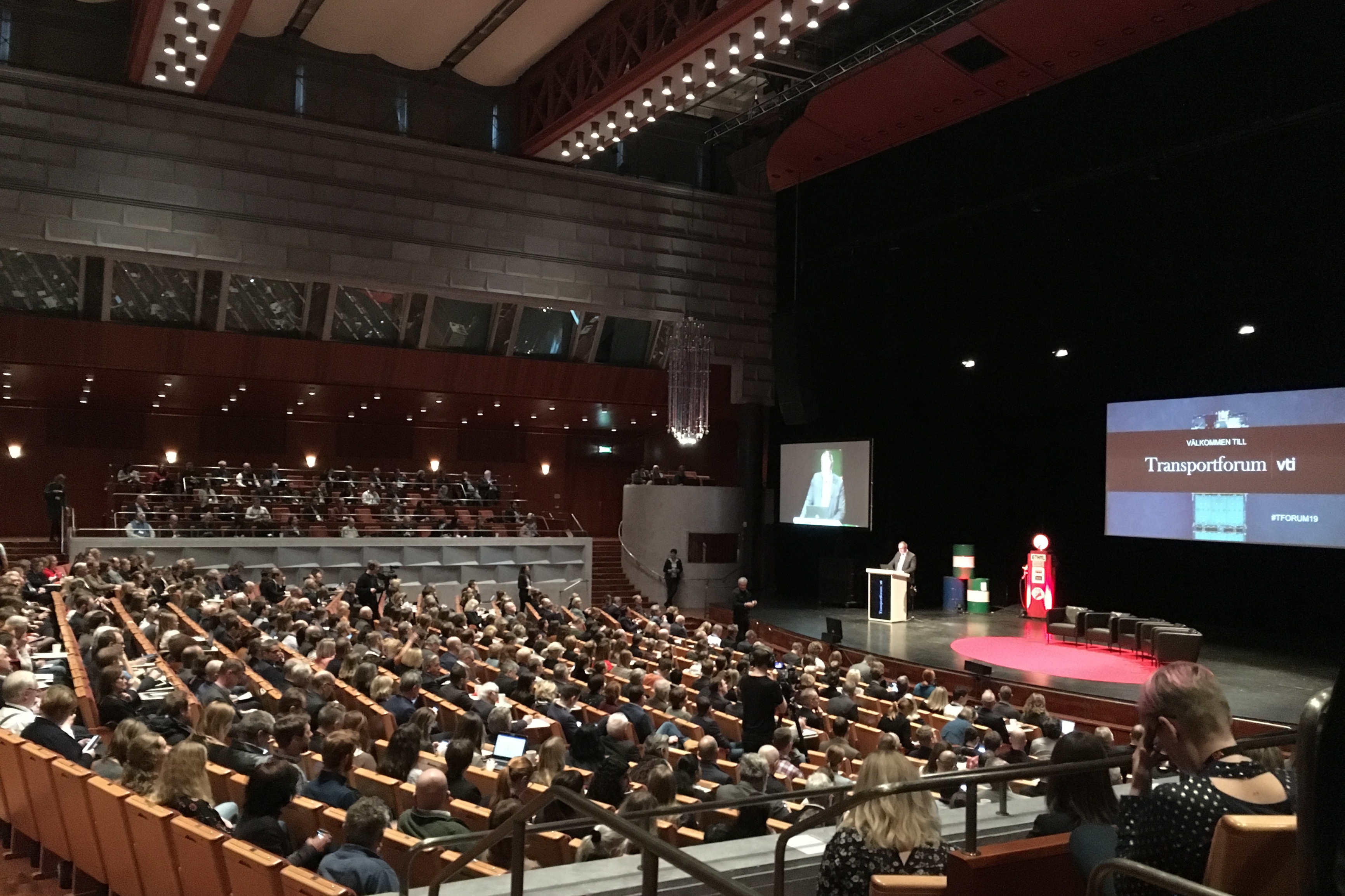 An auditorium, someone is on stage talking to a large audience.